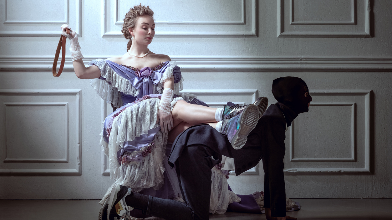 corporal punishment bdsm, well dressed woman holding a belt and sitting on a man