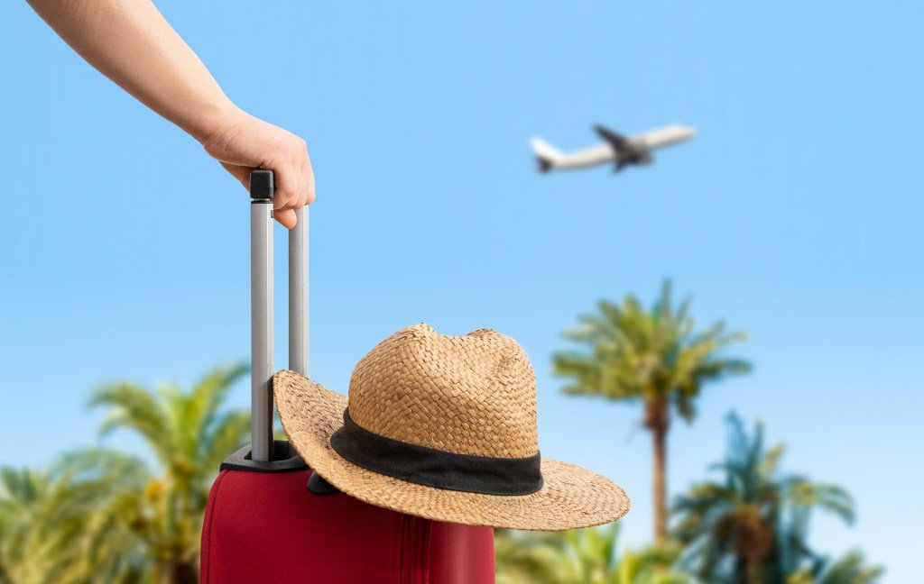 Woman with red suitcase standing on the passenger stairs of the plane, opposite the sea with palm trees, travel concept