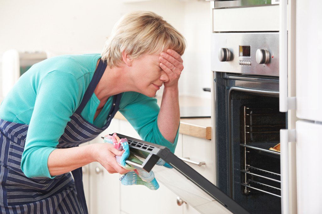 Woman covering her eyes looking at disastrous food in oven
