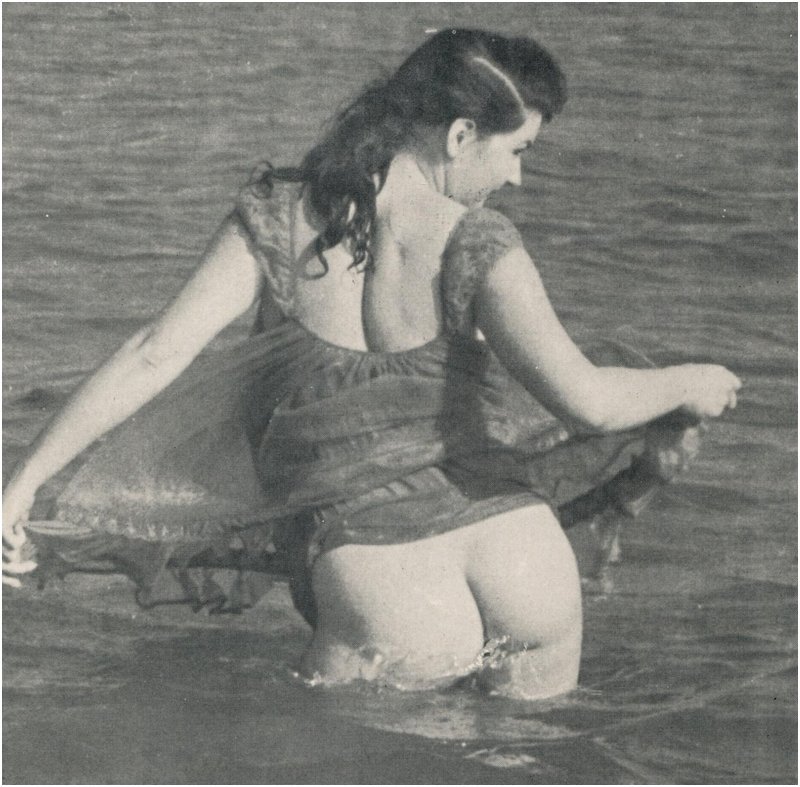 The 1950s bathing beauty's shower skirt on her cheek reveals her exposed bottom for the camera