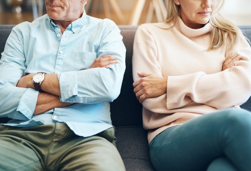 A couple sitting on the sofa with their arms crossed, looking unhappy.